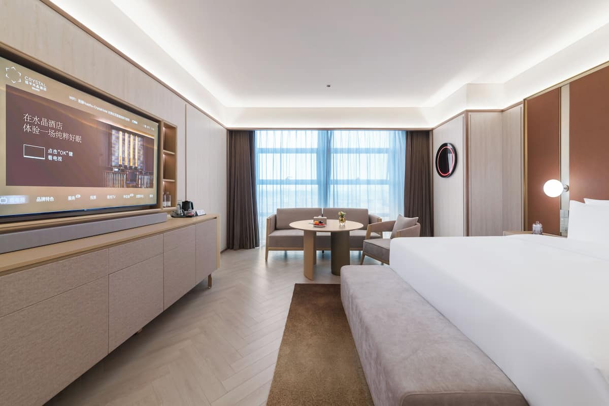Habitación de hotel con cama, escritorio, silla, televisión y ventana grande.