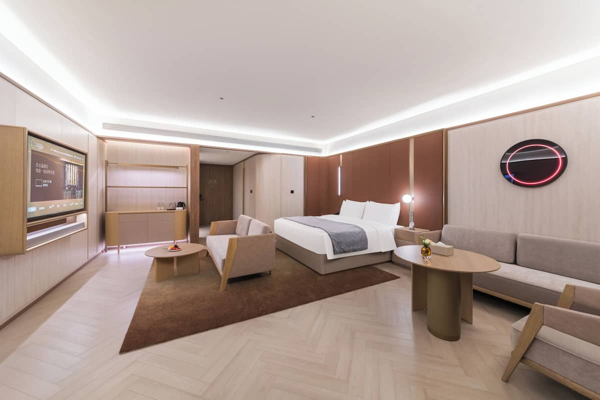 Moderni hotellihuone, jossa on sänky, sohva, nojatuoli ja televisio.