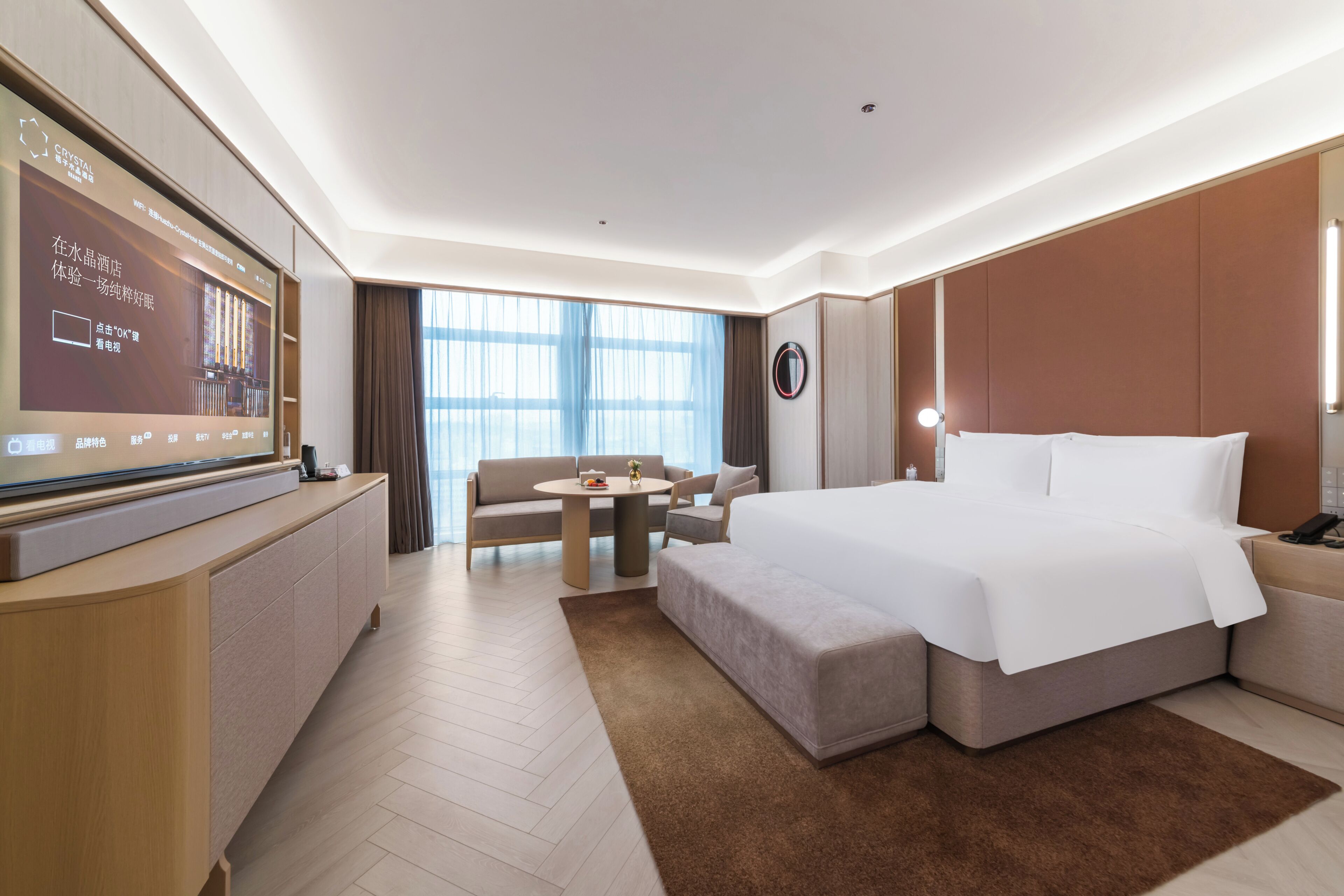 A hotel room with a bed, a desk, a TV, a sofa, and a large window.