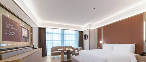 A hotel room with a bed, a desk, a TV, a sofa, and a large window.