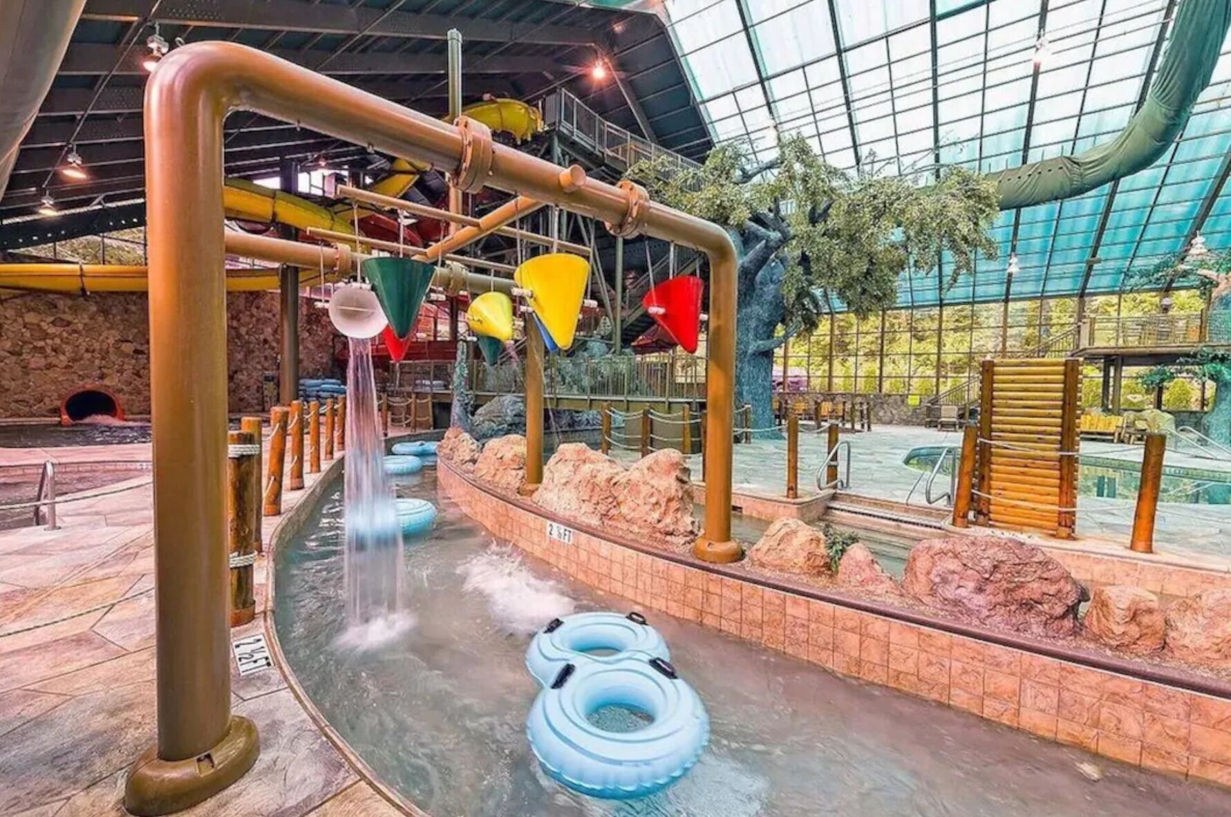 Un parc aquatique intérieur doté d’un toboggan aquatique, de bouées gonflables et d’un toit en verre.