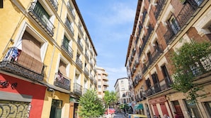 Una calle estrecha con edificios de varios pisos, balcones y coches aparcados.