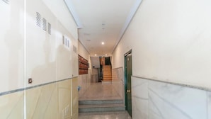 Un pasillo con suelo de mármol, una escalera y una puerta verde.