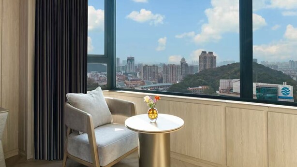 A modern room with a large window, a round table with a vase, a grey armchair, and a radiator.