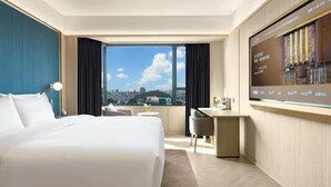 A hotel room with a large bed, a desk, a chair, and a TV screen.
