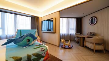 Habitación de hotel con cama, escritorio, silla, pequeña mesa, televisión y ventana con cortinas.