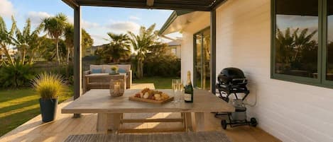 Un patio al aire libre con mesa de madera, asientos y una parrilla.
