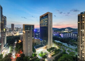 A modern hotel with a prominent glass facade, surrounded by urban high-rise buildings and a river.