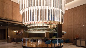 Um lobby moderno com um bar central, assentos e um lustre único.