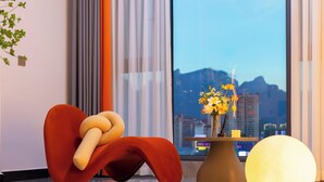 A modern room with a large window, a red chair, a round table with a vase of flowers, and a spherical light fixture. - Local Vibe Downtown Guesthouse (Zhangjiajie)