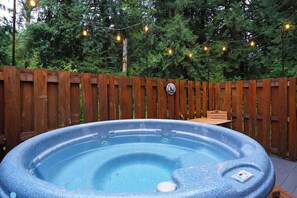 Un jacuzzi con muelle de madera y luces colgantes en un jardín.