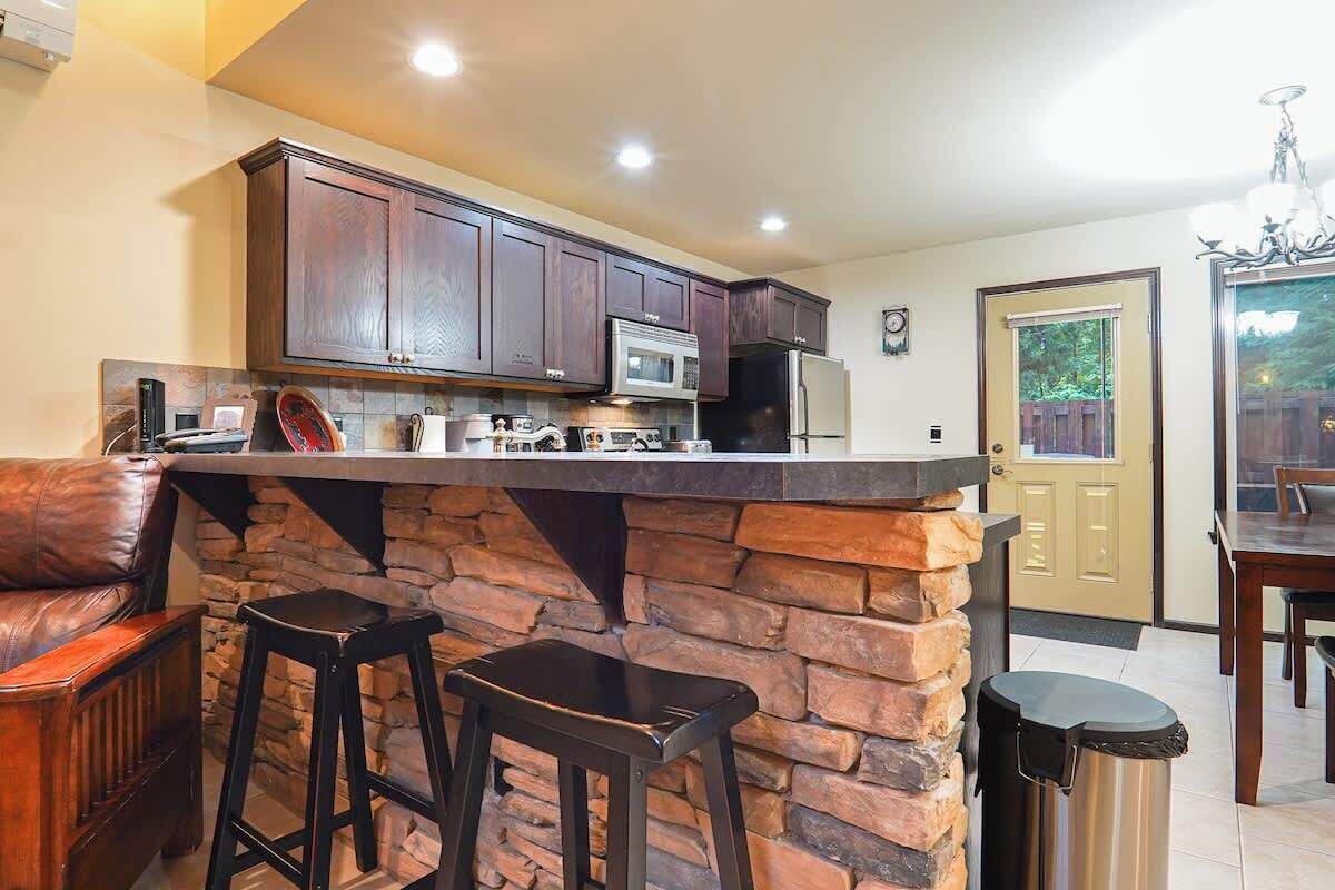 A kitchen with dark wooden cabinets, a stone accent wall, a built-in microwave, and a stainless steel refrigerator.