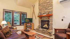 Ein gemütliches Wohnzimmer mit Kamin aus Stein, Ledermöbeln, einem Fernseher und einem Bücherregal.