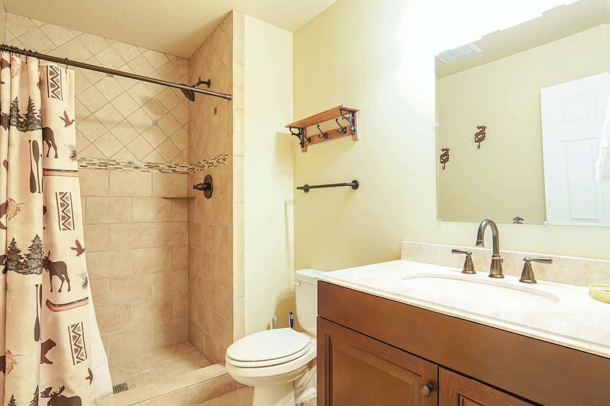 A bathroom with a shower, toilet, sink, and a mirror.