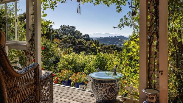 Een overdekt terras met uitzicht op een bergachtig landschap, rieten meubels en een decoratieve keramieken pot.