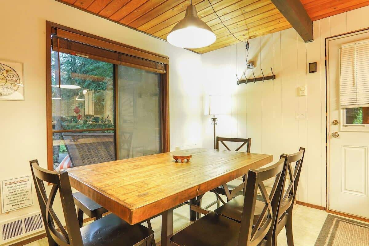 Een eethoek met een houten tafel en stoelen, een hanglamp, een schuifdeur met glas en een witte deur met raam.