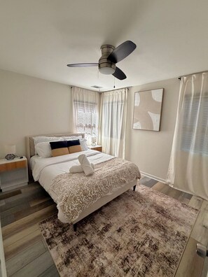 A bedroom with a bed, a ceiling fan, a nightstand, a lamp, a window with curtains, and a rug. - Charming 2-bedroom house in Atlanta perfect for relaxing (Atlanta)