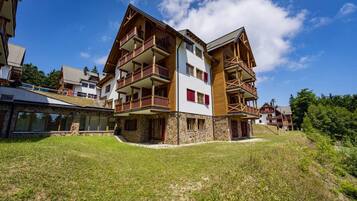 Un hôtel à plusieurs étages doté de balcons, d’une façade en pierre et surplombant une colline verdoyante.