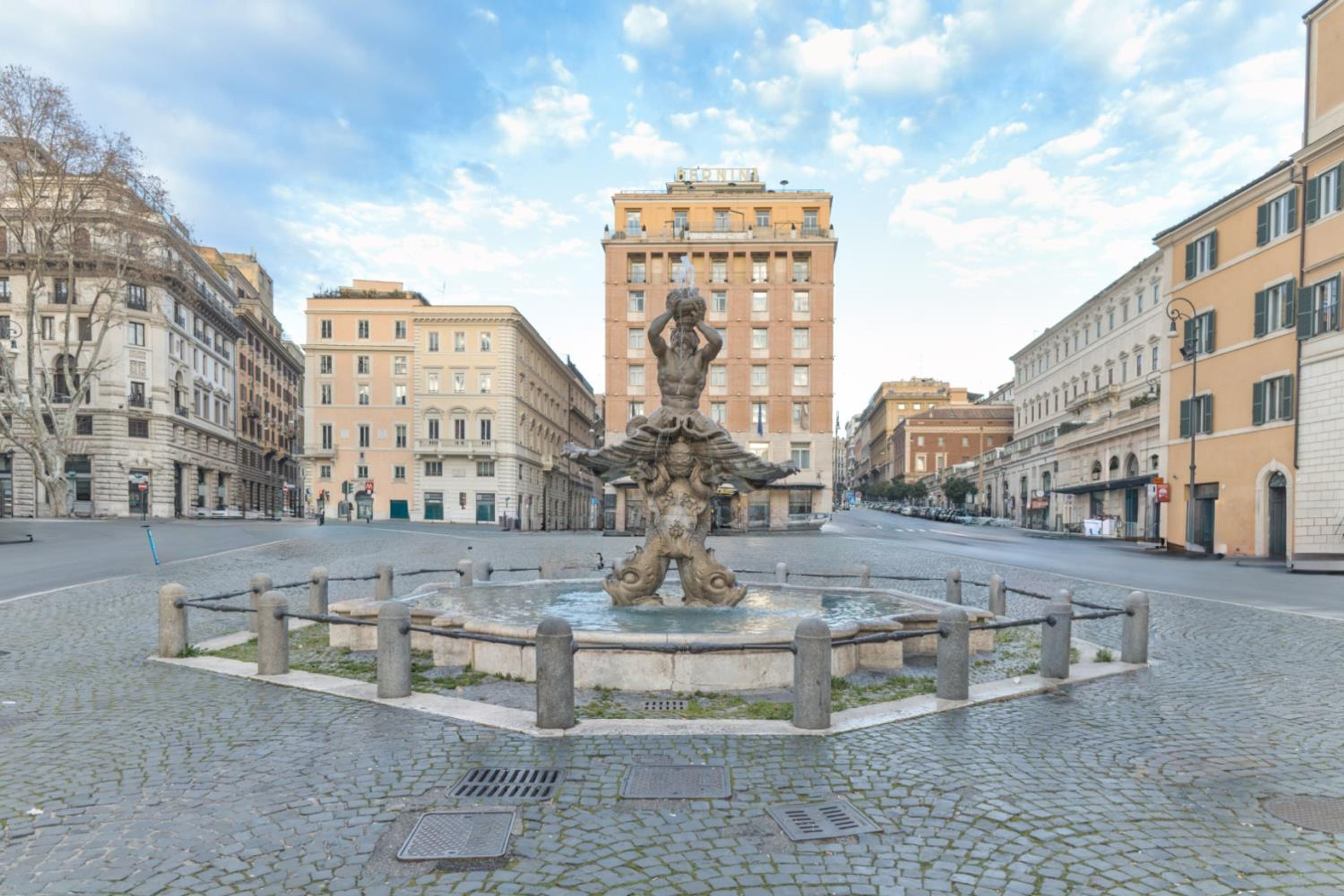 A square with a central fountain, cobblestone pavement, and surrounding historic buildings.