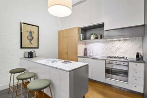 A modern kitchen with a marble countertop, wooden cabinets, a built-in oven, and a bar area with stools. - Chic 2-Bed Apartment in Melbourne CBD (Melbourne)