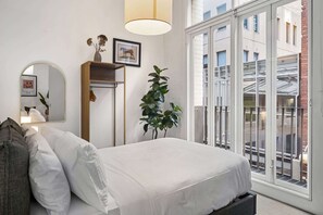 A bedroom with a bed, a mirror, a plant, and a window with a view of buildings. - Chic 2-Bed Apartment in Melbourne CBD (Melbourne)