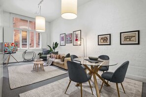 A modern living room with a glass table, dark chairs, a sofa, and artwork on the walls. - Chic 2-Bed Apartment in Melbourne CBD (Melbourne)