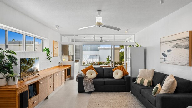 A modern living room with a black sofa, wooden entertainment unit, and a large window. - Resort-Style Apartment Steps from Dining, Beach & Marina in Port Douglas (Port Douglas)