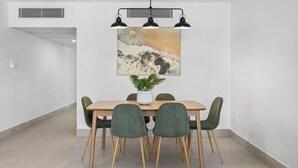 A dining area with a wooden table, green chairs, a potted plant, and a painting above. - Resort-Style Apartment Steps from Dining, Beach & Marina in Port Douglas (Port Douglas)