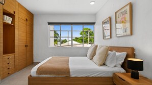 A bedroom with a bed, wooden wardrobe, window, and wall art. - Resort-Style Apartment Steps from Dining, Beach & Marina in Port Douglas (Port Douglas)