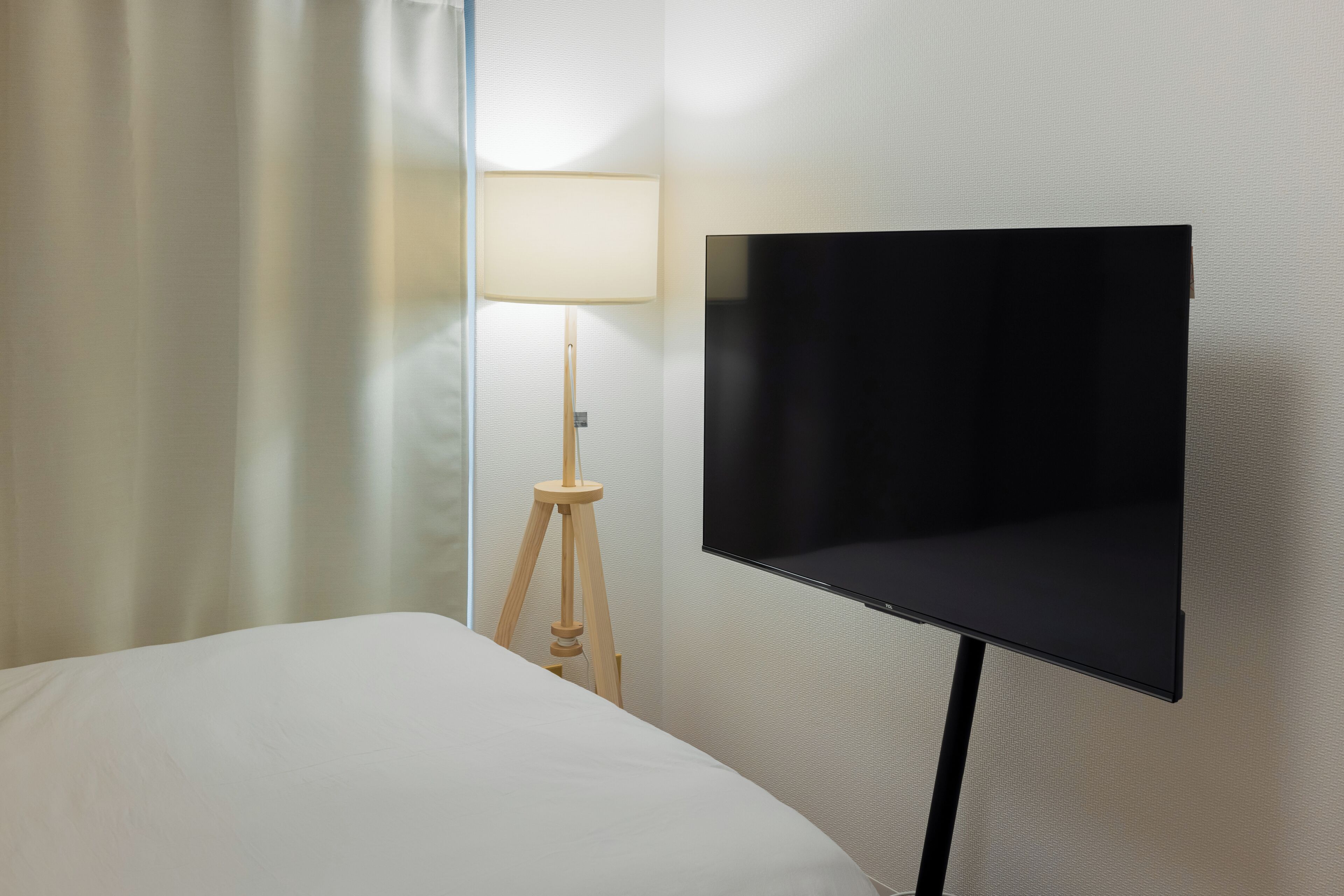 A hotel room with a bed, a wall-mounted TV, and a lamp.
