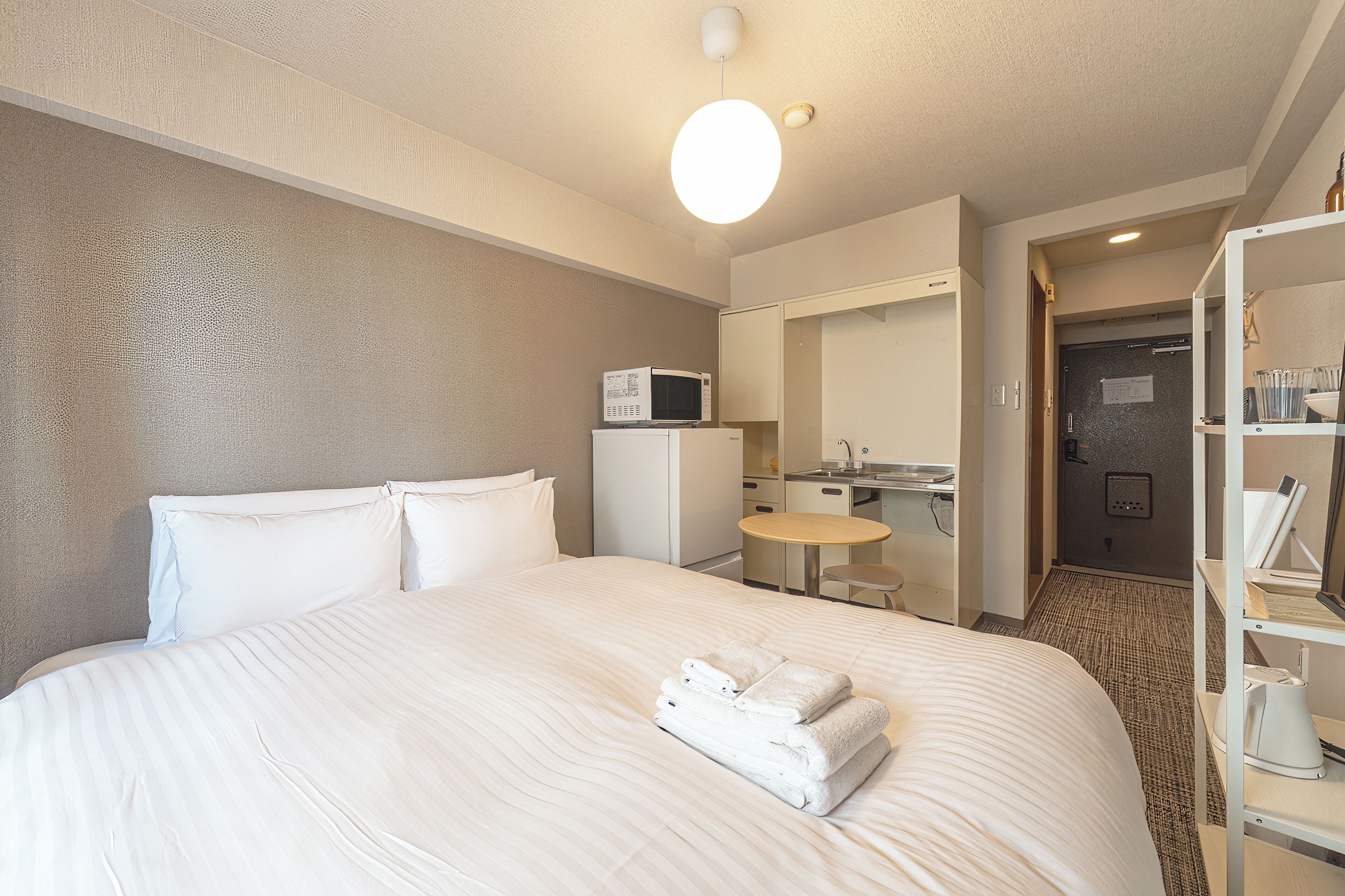 A hotel room with a large bed, a microwave, a small table, and a bathroom visible through an open door.