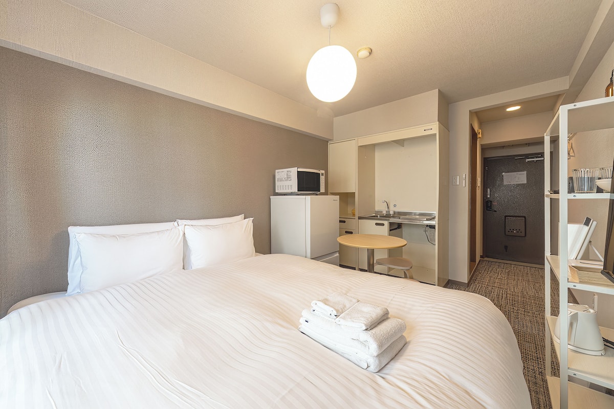 A hotel room with a large bed, a microwave, a small table, and a bathroom visible through an open door.