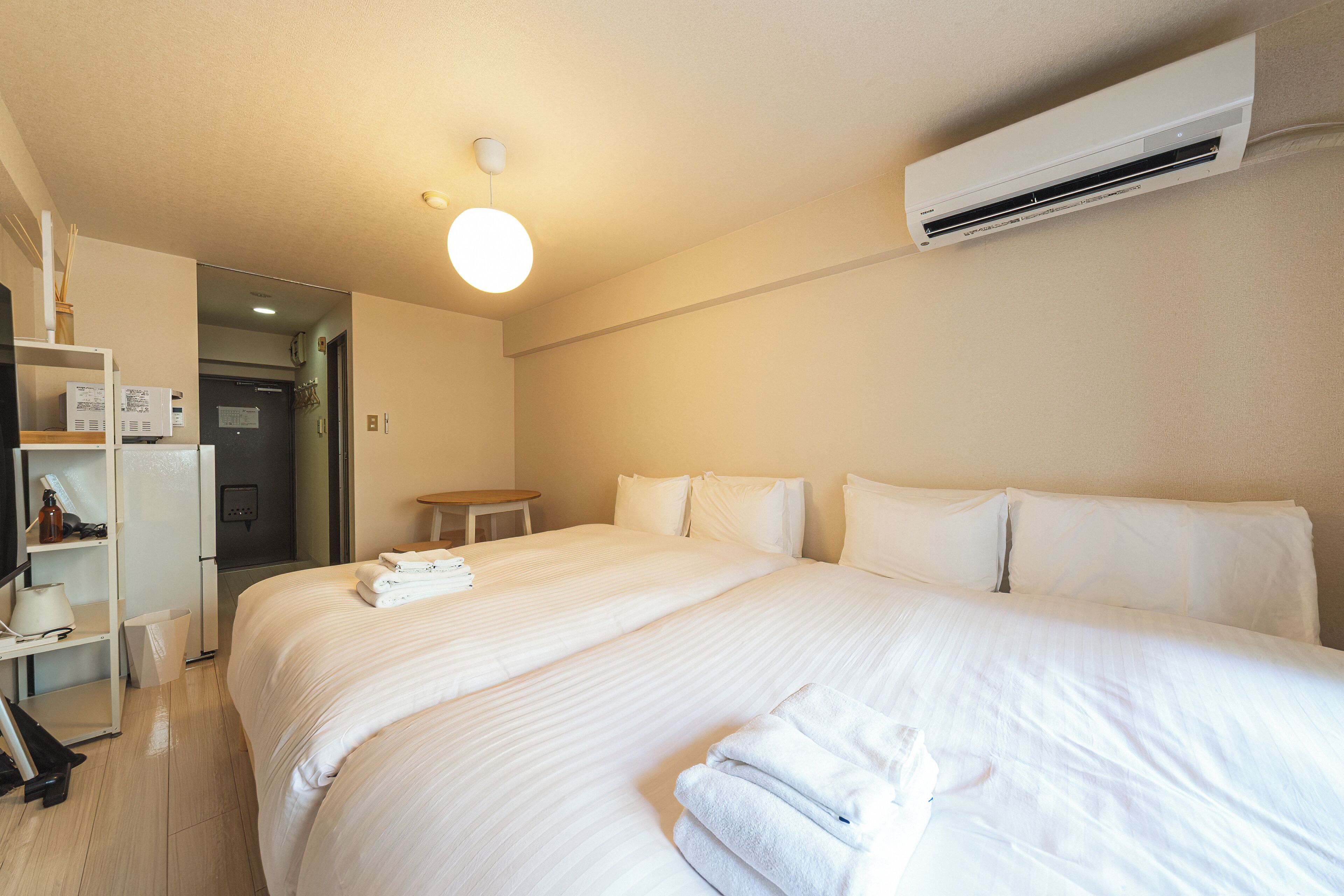 A hotel room with a large bed, a small table, a wardrobe, and an air conditioning unit.