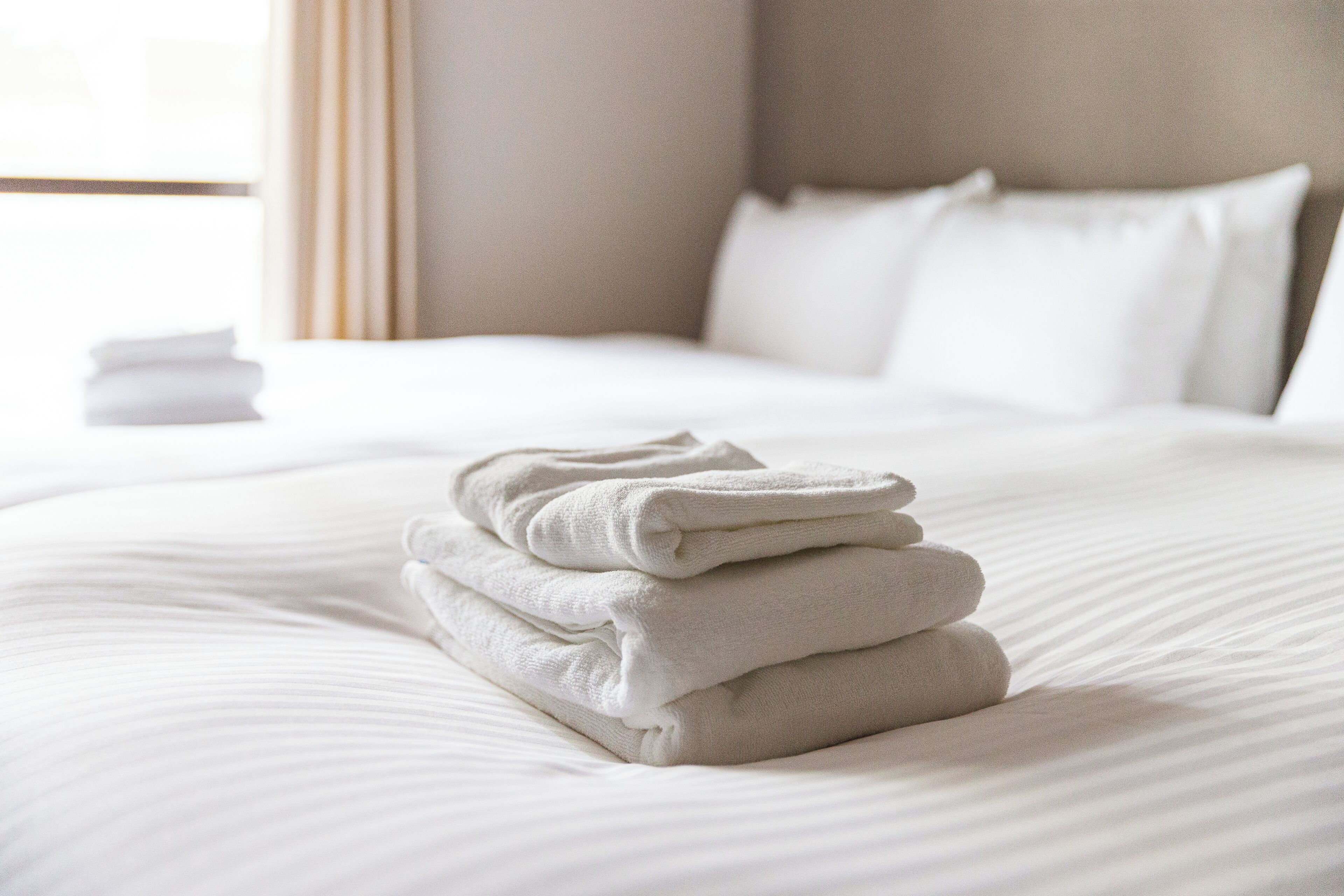 A neatly made bed with folded towels and a stack of white towels on the side.