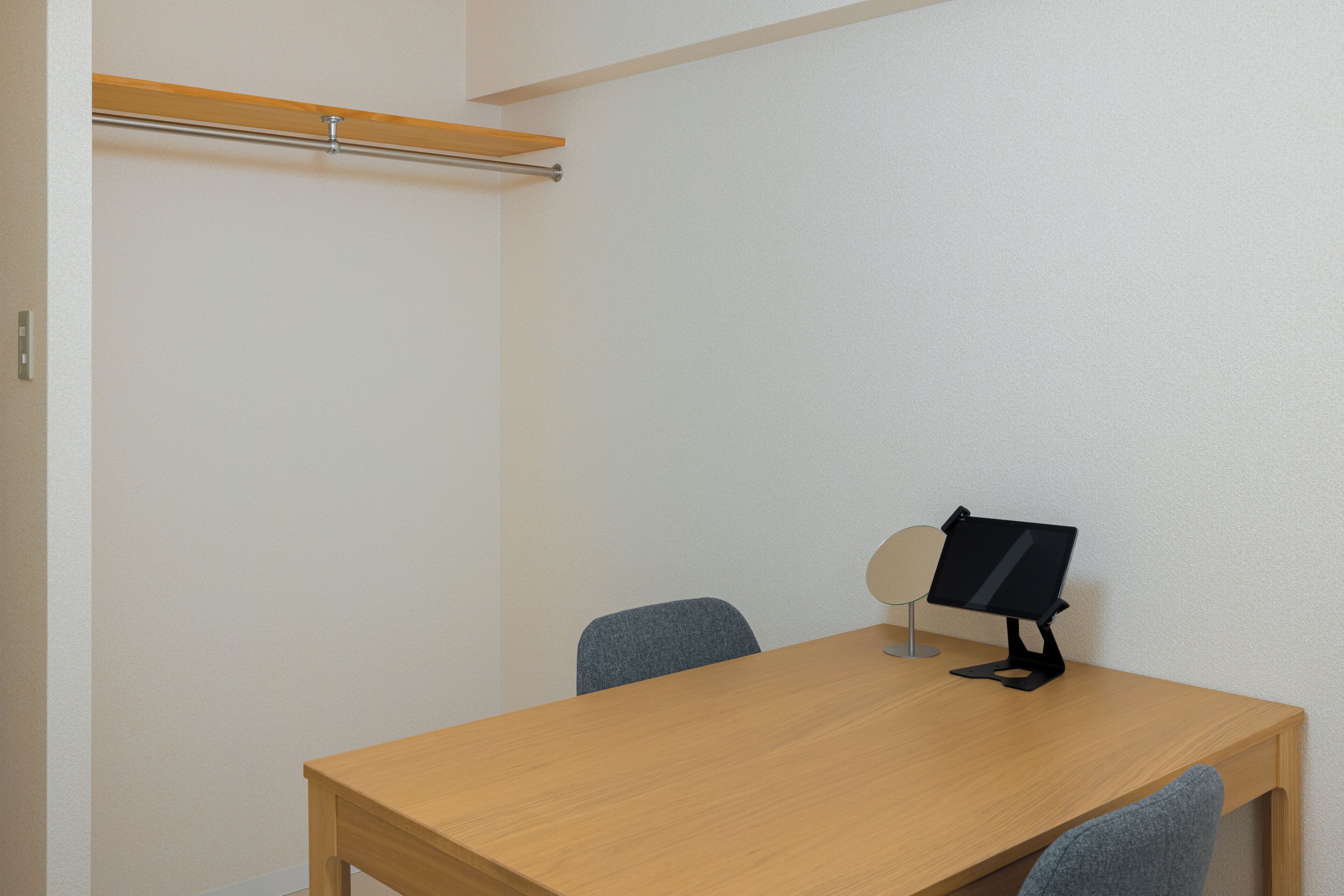 Um quarto com uma mesa de madeira, duas cadeiras, um suporte para partituras e um cabideiro.