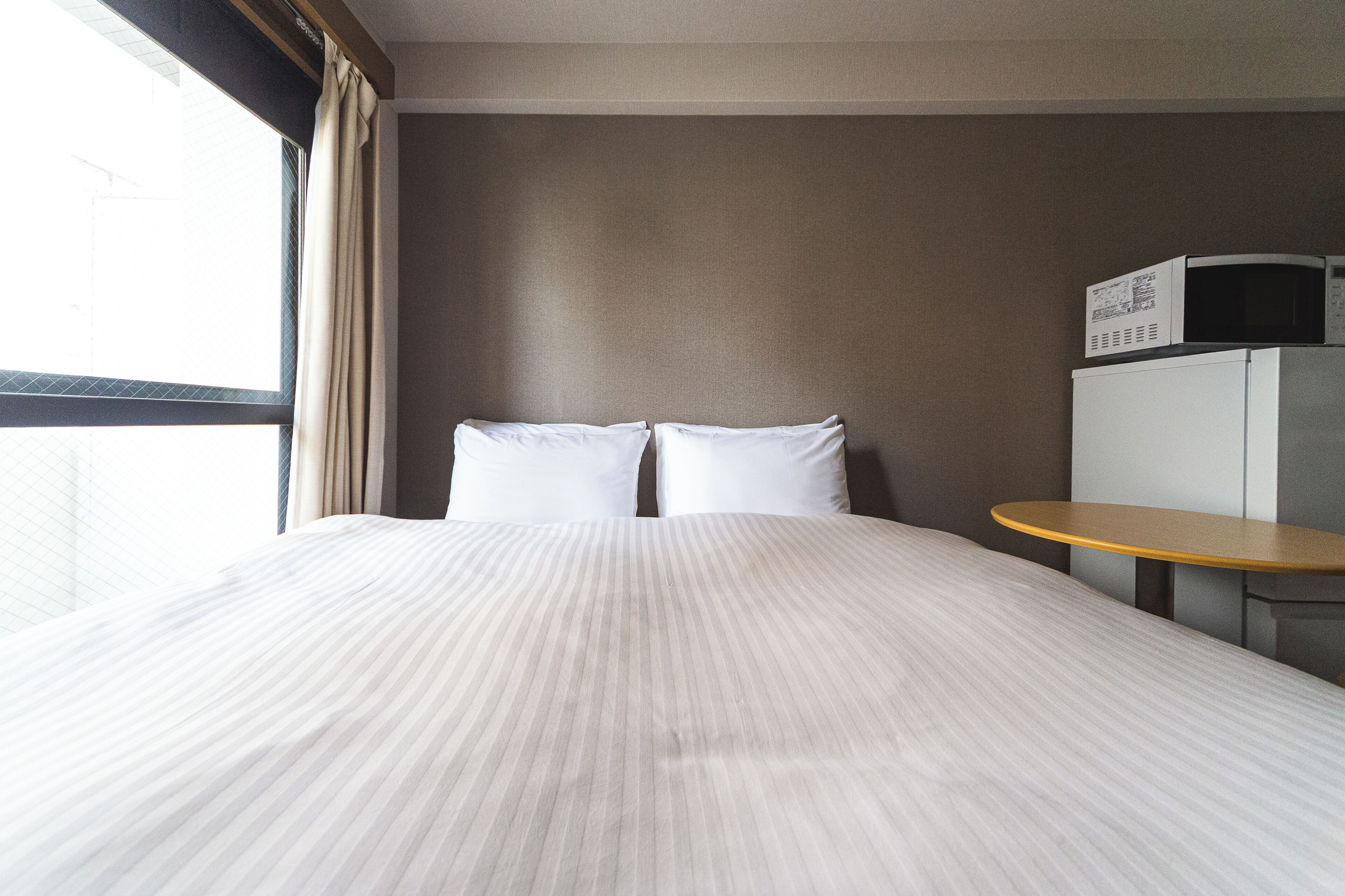 Una habitació d'hotel amb un llit, almoines, una taula petita i un microones damunt d'un moble.