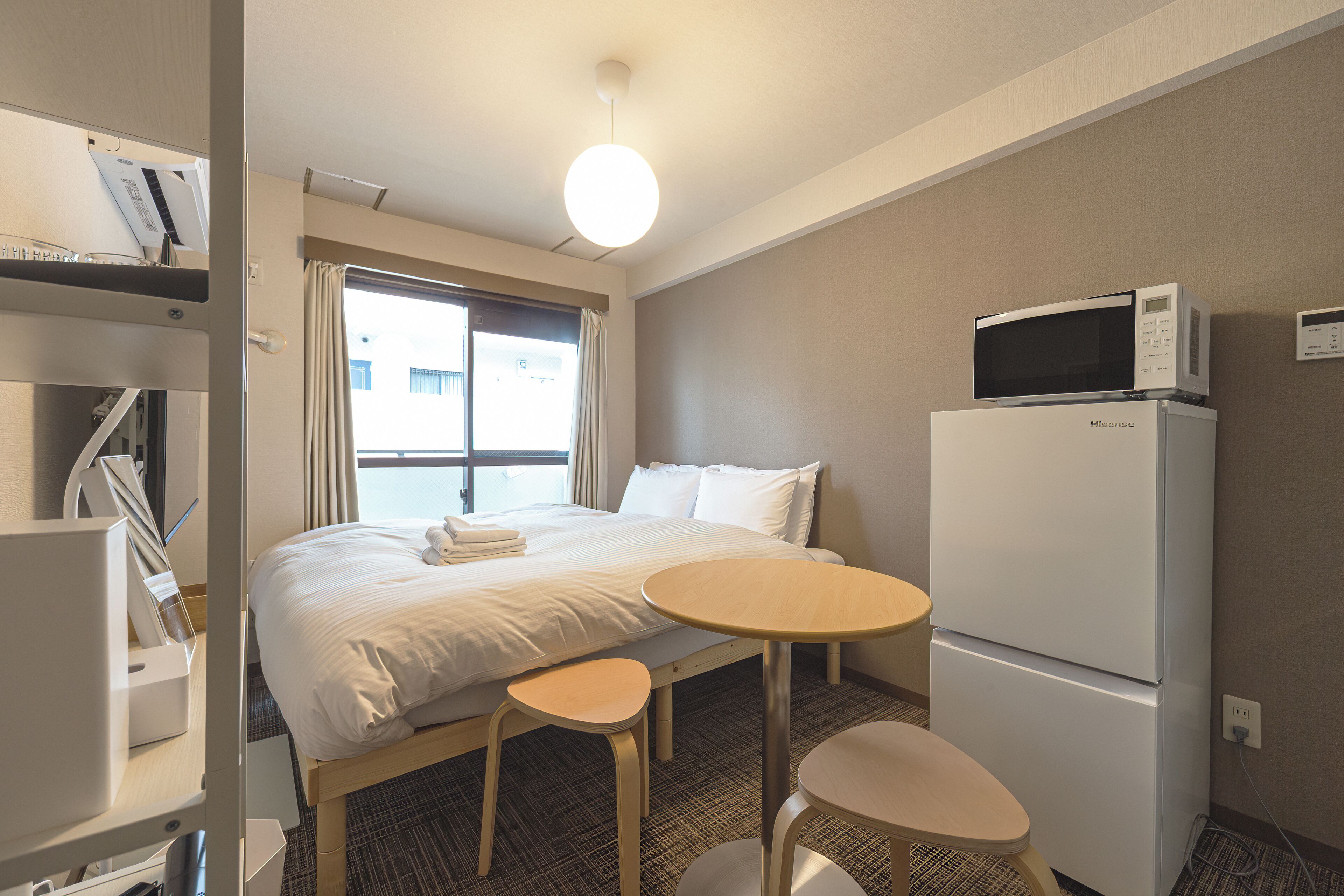 A hotel room with a bed, a desk, two chairs, a microwave, and a refrigerator.