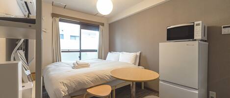 A hotel room with a bed, a desk, two chairs, a microwave, and a refrigerator.