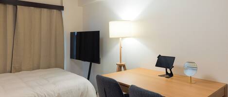 A hotel room with a bed, a desk with a lamp, a TV, and a small table with a mirror.