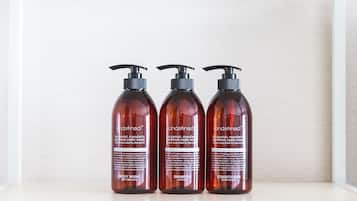 Trois bouteilles de gel douche, de shampoing et d’après-shampoing de la marque Undefined sont posées sur une étagère.