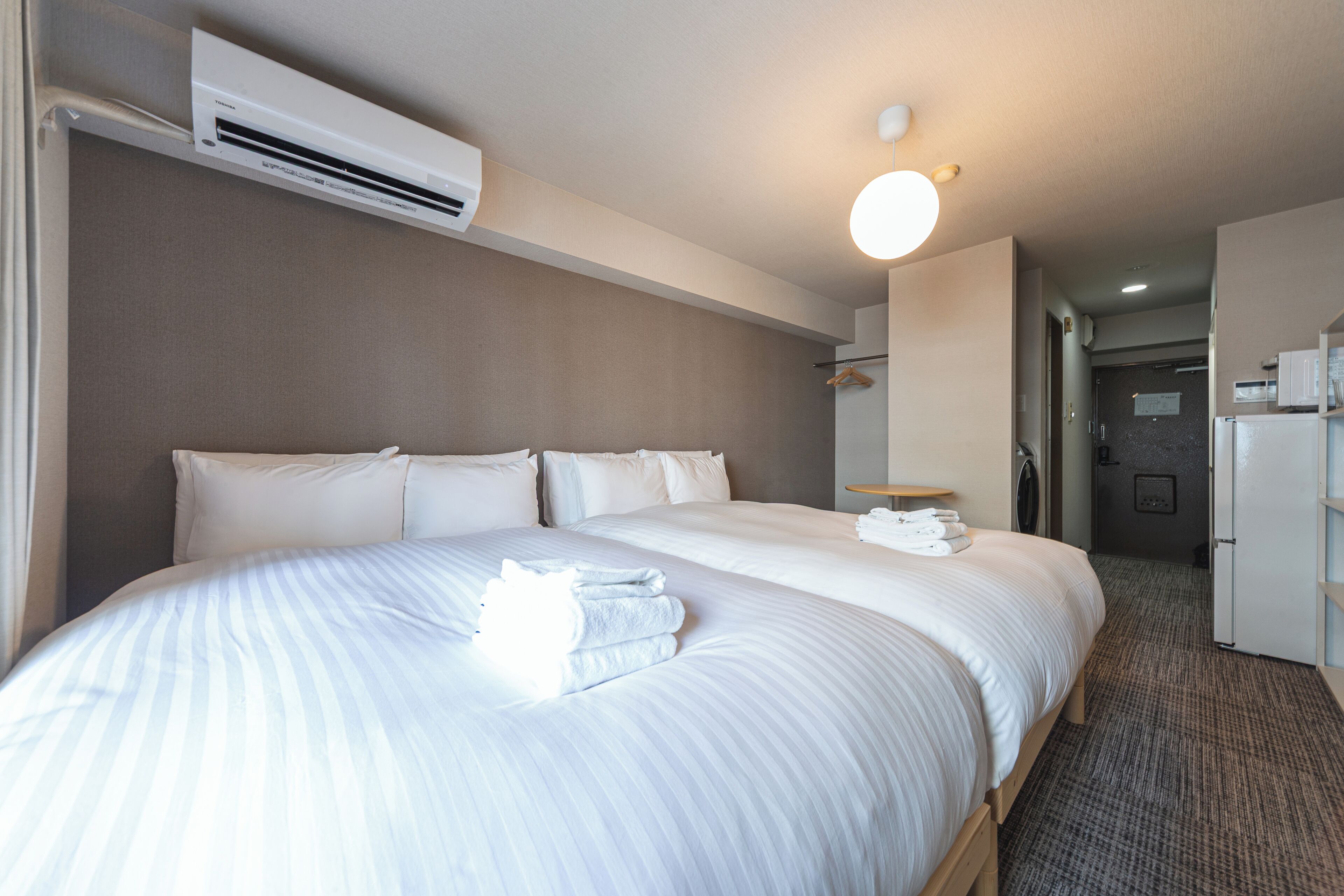 A hotel room with a large bed, an air conditioning unit, a bedside table, a mirror, and a door leading to a bathroom.