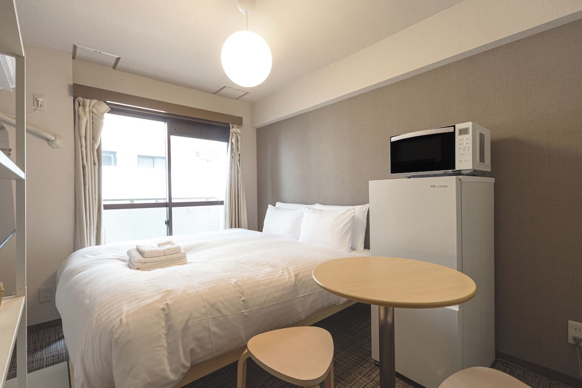 A hotel room with a bed, a microwave, a table, and a chair.
