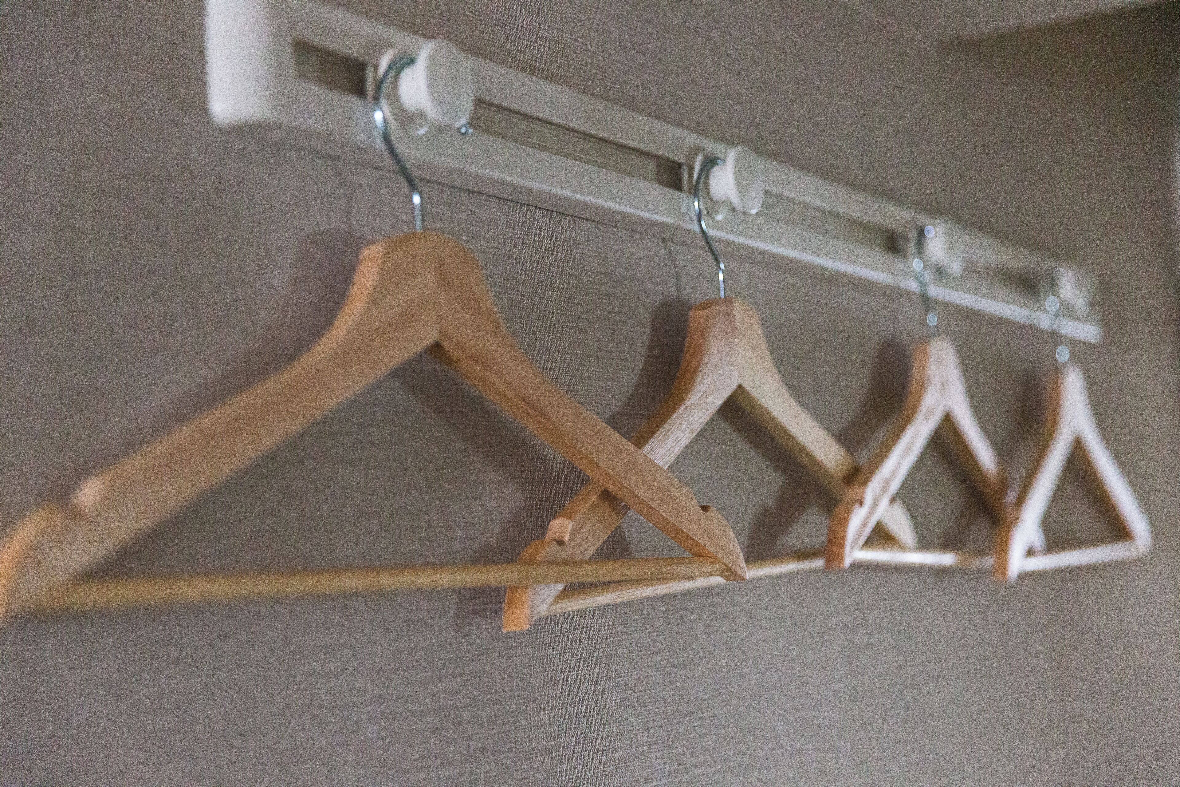 Un portant à vêtements avec des cintres en bois, placé contre un mur à texture.