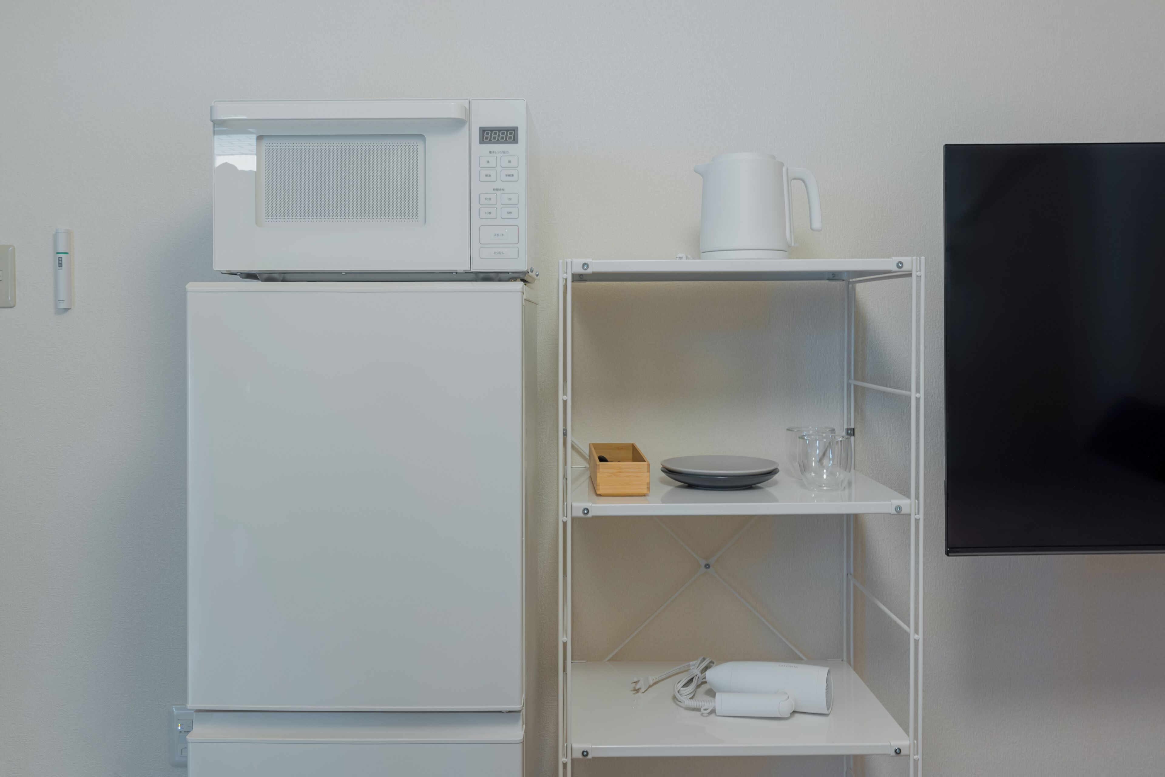 A white refrigerator, a microwave, a white shelf with a cup, a bowl, and a glass.