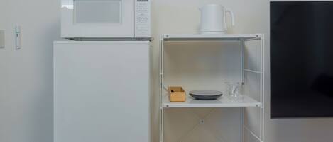 A white refrigerator, a microwave, a white shelf with a cup, a bowl, and a glass.