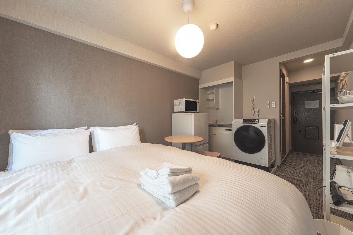 A hotel room with a bed, a washing machine, a microwave, and a small table.