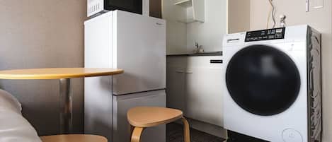 A compact hotel room with a kitchenette, a microwave, a refrigerator, a washing machine, and a small wooden table.