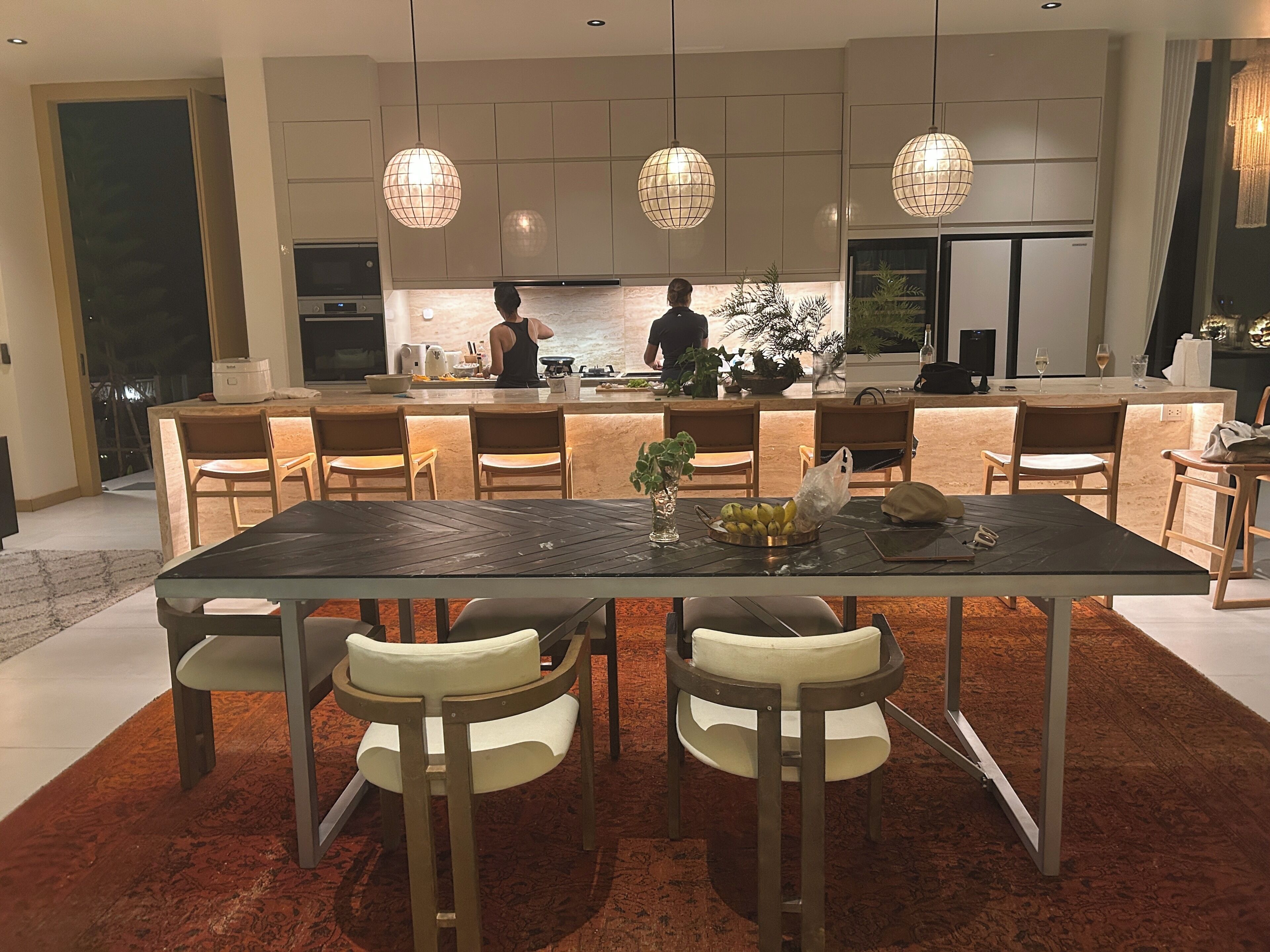 A modern kitchen with a central island, pendant lighting, and a dining area with a table and chairs.