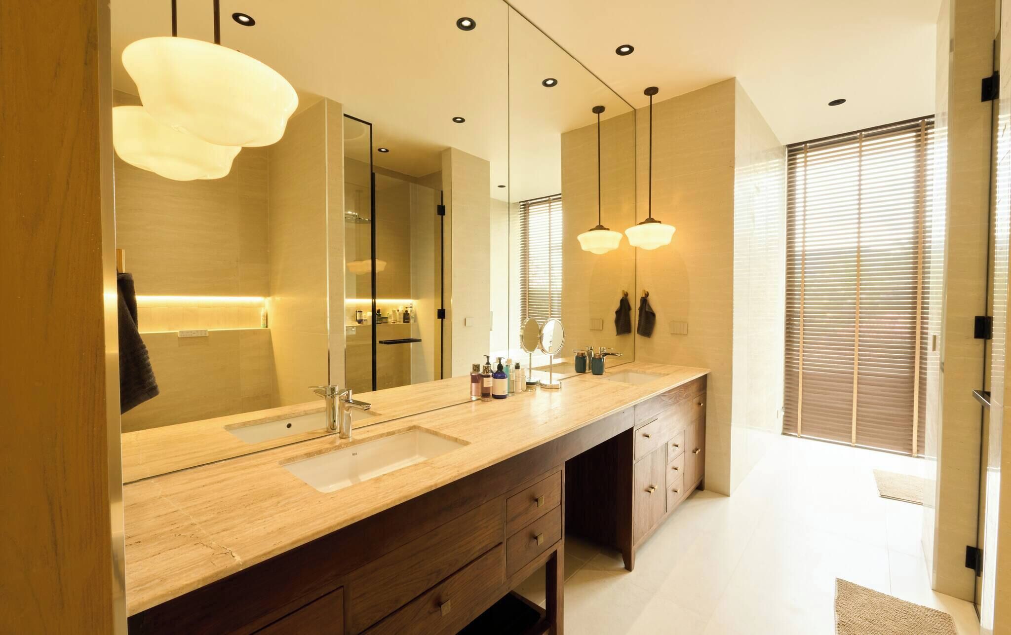 A modern bathroom with a large mirror, dual sinks, and pendant lighting.