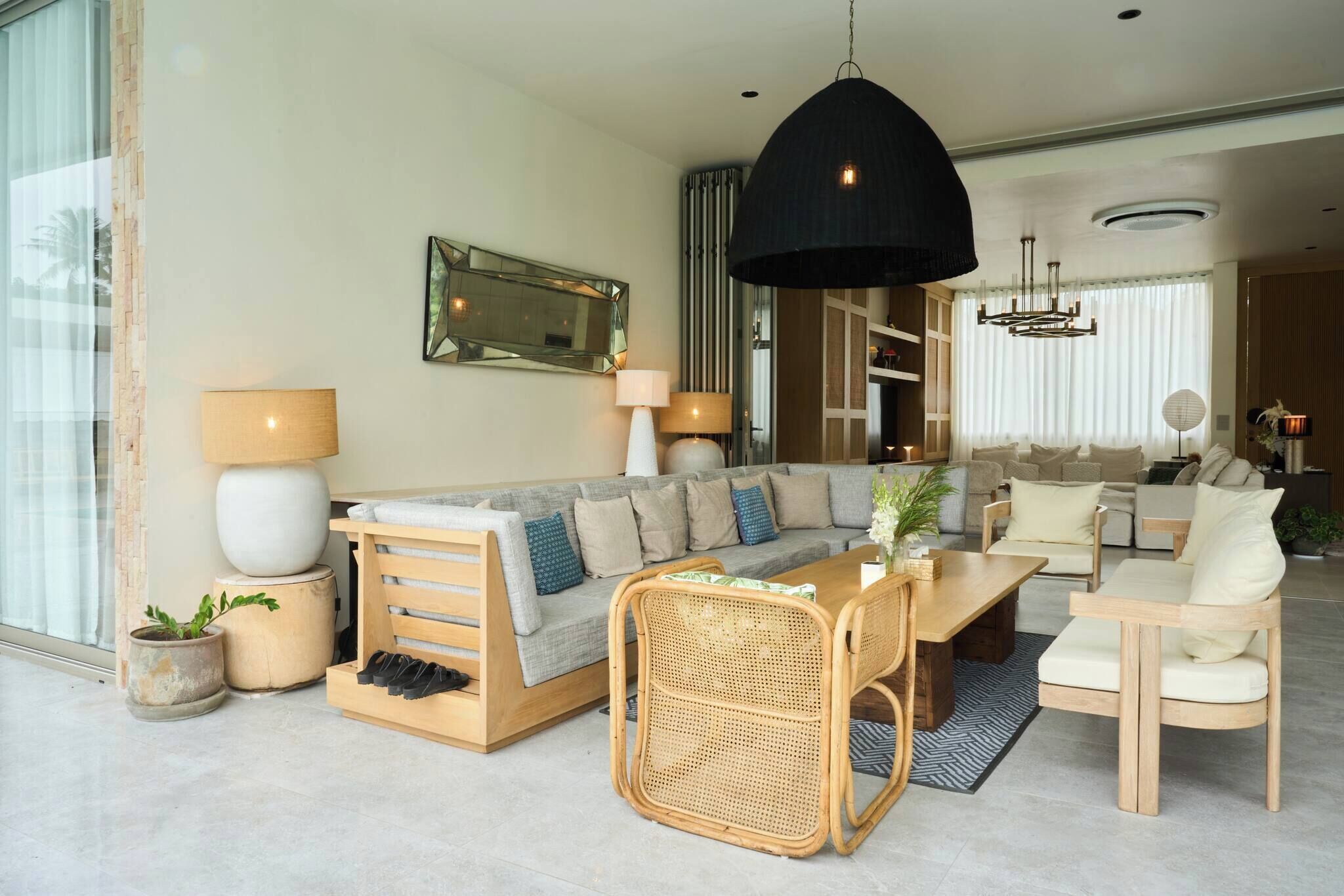 A modern living room with a sofa, a dining table, and chairs. There is a large mirror on the wall and a hanging light fixture.